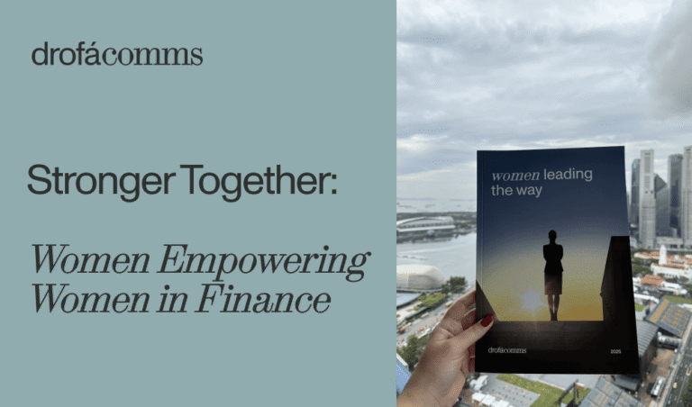 A hand holds the Women Leading the Way magazine on the gender gap in fintech, with a Singapore skyline at dusk